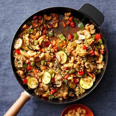 a skillet filled with vegetables and nuts next to a bowl of sauce on the side