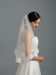 a woman in a white wedding dress with a veil on her head is looking down