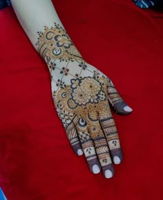 a henna on someone's hand that is sitting on a red blanket