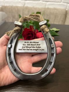 a hand holding a metal horseshoe with a red rose in the center and a card attached to it