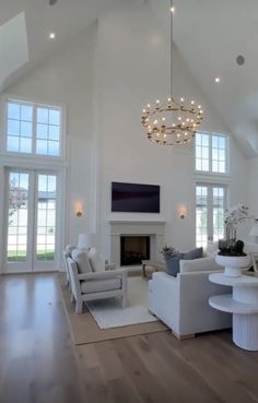 a living room filled with furniture and a chandelier hanging from the ceiling in front of two large windows