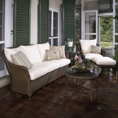 two wicker couches sitting on top of a wooden floor next to green shutters