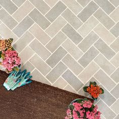 some flowers are sitting on the ground next to a tile wall that has herringbone pattern