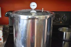 a stainless steel pressure cooker sitting on top of a black stove with a clock above it