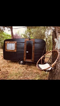 a small black trailer parked next to a tree in the woods with a swing chair on it