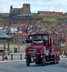 a red bus driving down a street next to a tall castle on top of a hill