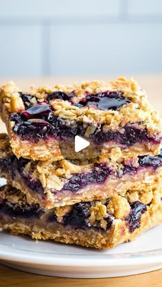 blueberry crumble bars stacked on top of each other in front of a white plate