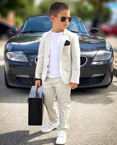 a young man is standing in front of a car holding a briefcase and wearing sunglasses