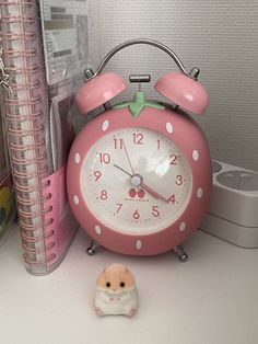 a pink alarm clock sitting on top of a desk next to a small toy mouse