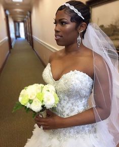 a woman in a wedding dress holding a bouquet and looking at the camera while standing on a long hallway