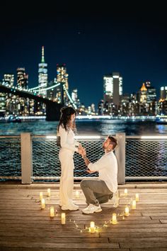 a man kneeling down next to a woman on top of a wooden deck near the water