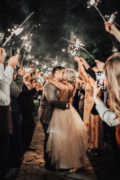 a bride and groom kiss as they hold sparklers in front of their wedding guests