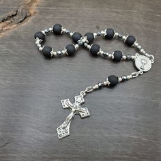 Channel of Peace's rosaries and chaplets are made by hand with prayerful hands in the United States. Additional details: Crucifixlvertone crucifix Center: silvertone, single-sided Holy Communion center Our Father/Hail Marys: 6mm matte black glass beads Accents: silvertone bead caps Spacers and accents:  3mm grey metallic Czech fire glass beads 3mm metal spacer beads Wire used- 49 strand beading wire Components- crimp beads, jump rings, wire protectors All of our handmade rosaries, chaplets, and more are made with prayerful hand in the United States. All items ship in a waterproof bubble mailer, with waterproof shipping labels.  Currently Shipping on- please check shipping times Black Rosary, One Decade Rosary, Mens Rosary, Rings Wire, Pocket Rosary, Decade Rosary, Crimp Beads, Fire Glass, Rosary Catholic