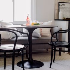 a table with two chairs and a bottle on it in front of a couch that is next to a window