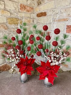 two silver vases filled with red flowers and greenery