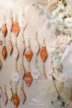 many different colored tags hanging on a wall next to some white and pink flowers in the background