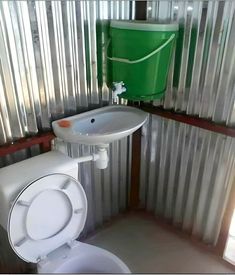 a white toilet sitting next to a green trash can on top of a metal wall