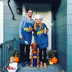 two people in blue aprons standing on the steps with a dog wearing an apron