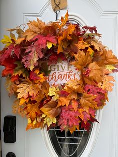 a wreath that says give thanks hanging on the front door with fall leaves around it