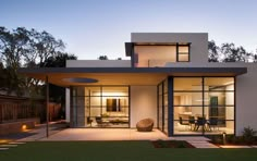 a modern house is lit up at night with lights on the windows and patio area