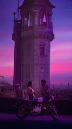 two people sitting on a motorcycle in front of a tower