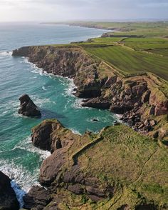 an aerial view of the ocean and coastline near rocky cliffs with grass growing on them