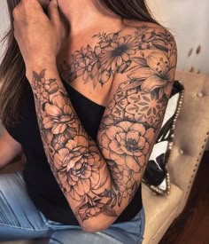 a woman sitting on top of a couch holding her hand up to her face with flowers all over her arm