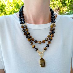 Tiger eye and black onyx layered necklace with pendant. Chunky statement natural gemstone beaded necklace for women. Large brown black handmade necklace with big bead and gemstone. Big bold bohemian bright necklace in gold color are suitable for an casual look, evening look and for a holiday. These necklace will be a good Mothers day, anniversary, wedding or birthday gift for women, mom, wife, girlfriend, sister or daughter. Women's necklace with natural stone. It emphasizes the beauty of your neck and adds charm to your look. FAST FREE SHIPPING EARRINGS AS A GIFT You can see even more necklace here.   https://www.etsy.com/shop/VesnekaJewelry?ref=seller-platform-mcnav§ion_id=40601375 Dimensions: The short necklace has a length of 50 centimeters. Structure: Tiger eye, black onyx, hematite, Handmade Black Necklace For Layering, Black Handmade Necklace For Layering, Bright Necklace, Tiger Eye Necklace, Large Bead Necklace, Gemstone Pendant Necklace, Tigers Eye Necklace, Gemstone Beaded Necklace, Jewelry Statement