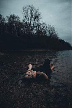 a woman laying on her back in the water with trees in the background at night