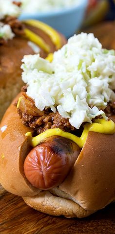 two hot dogs with mustard, onions and cheese on them sitting on a cutting board