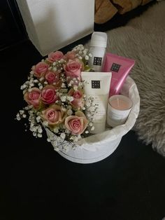 a white basket filled with lots of pink flowers next to a candle and some other items