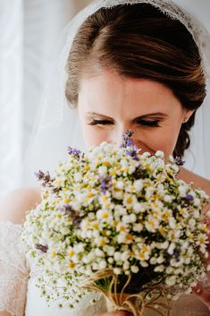 a woman in a wedding dress holding a bouquet of white and yellow flowers with her eyes closed