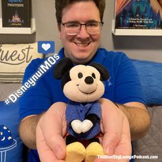 a man holding a mickey mouse stuffed animal in his hands and smiling at the camera