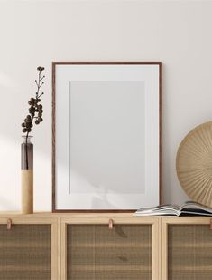 an empty frame on top of a wooden shelf next to a vase with flowers in it