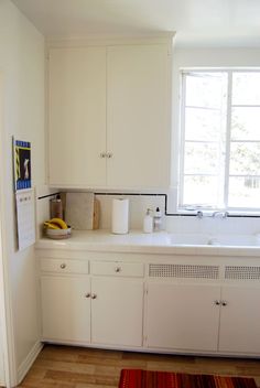 a kitchen with white cabinets and wooden flooring next to a window in the wall