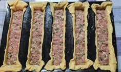 four uncooked pizza doughs lined up on a baking sheet, ready to go into the oven