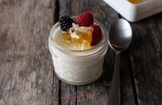 a dessert in a small glass jar with fruit on top and two spoons next to it