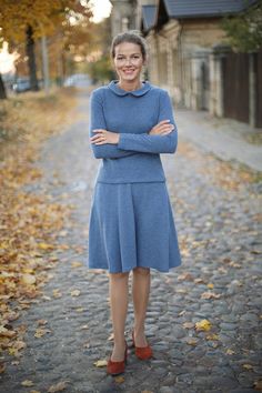 a woman standing on a cobblestone road wearing a blue dress with her arms crossed