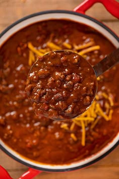 a ladle full of chili and cheese on top of a wooden table with a spoon