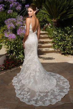 a woman in a white wedding dress standing on a stone path with purple flowers behind her