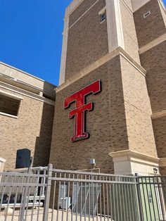 a tall brick building with a red t sign on it's front entrance and gate