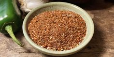 a bowl filled with ground spices next to green peppers and garlic on a wooden table