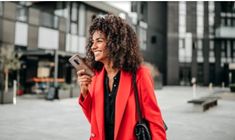 a woman with curly hair is holding a cell phone in her hand and smiling at the camera