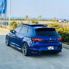 a blue car parked in front of a building near the ocean and palm trees,