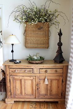 a wooden cabinet with a basket on top and flowers in the middle, next to a lamp