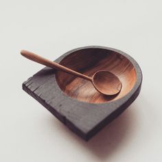 a wooden bowl with a spoon in it on top of a black coaster and white background