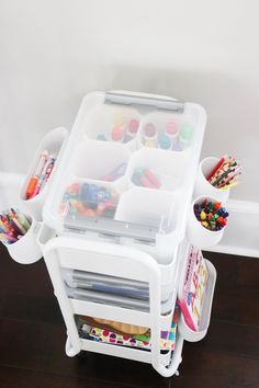 two plastic storage containers filled with art supplies on top of a hard wood floor next to a white wall