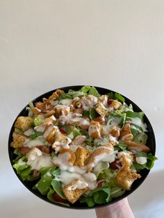 a hand holding a black bowl filled with salad