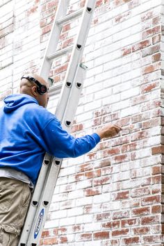 a man in blue jacket standing on ladder next to brick wall