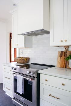 a kitchen with white cabinets and stainless steel stove top oven, dishwasher and cutting board on the counter